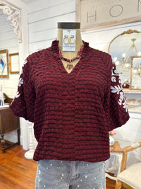 Maroon textured sweater with white patterns on a mannequin in a store setting.