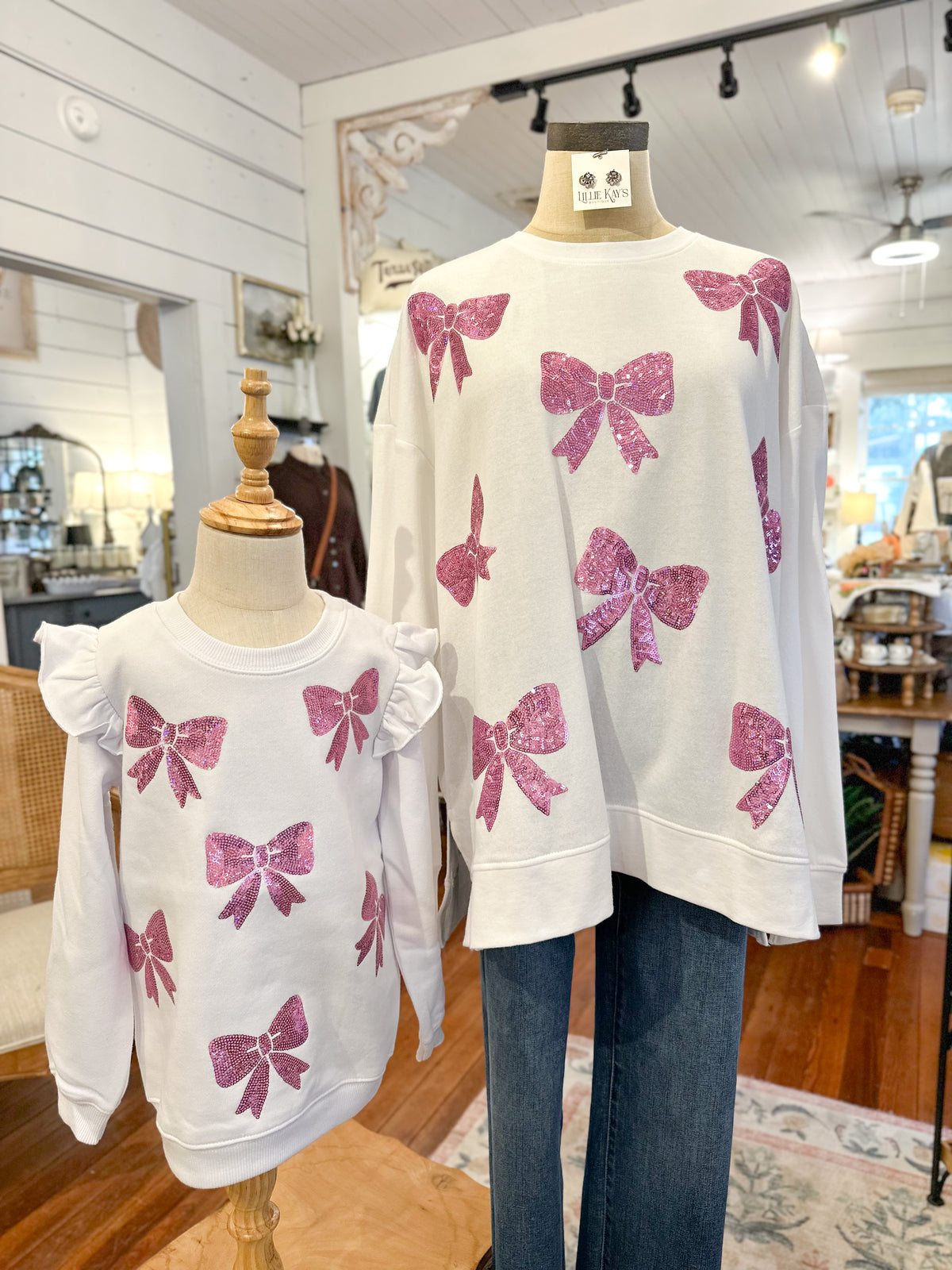 White sweaters with pink bow patterns on mannequins in a store setting.