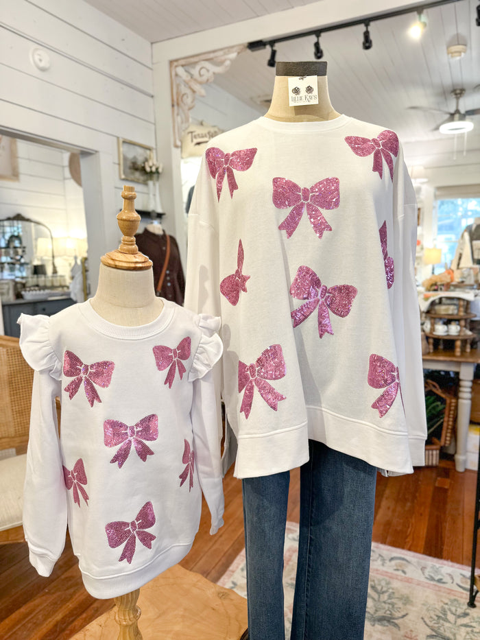 White sweaters with pink bow patterns on mannequins in a store setting.