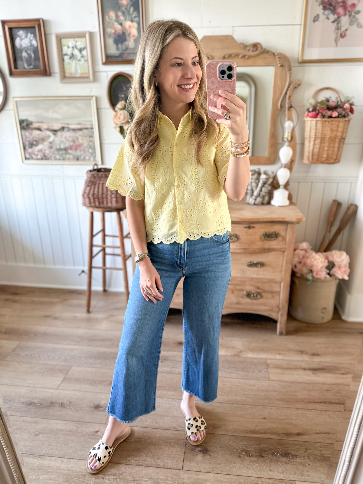 Woman taking a mirror selfie wearing a yellow lace blouse and blue jeans in a home setting.