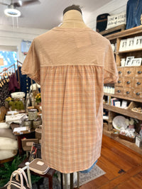 A short-sleeve top displayed on a mannequin in a boutique, featuring a solid mauve upper back and shoulders with a peach and brown plaid patterned lower back and skirt.