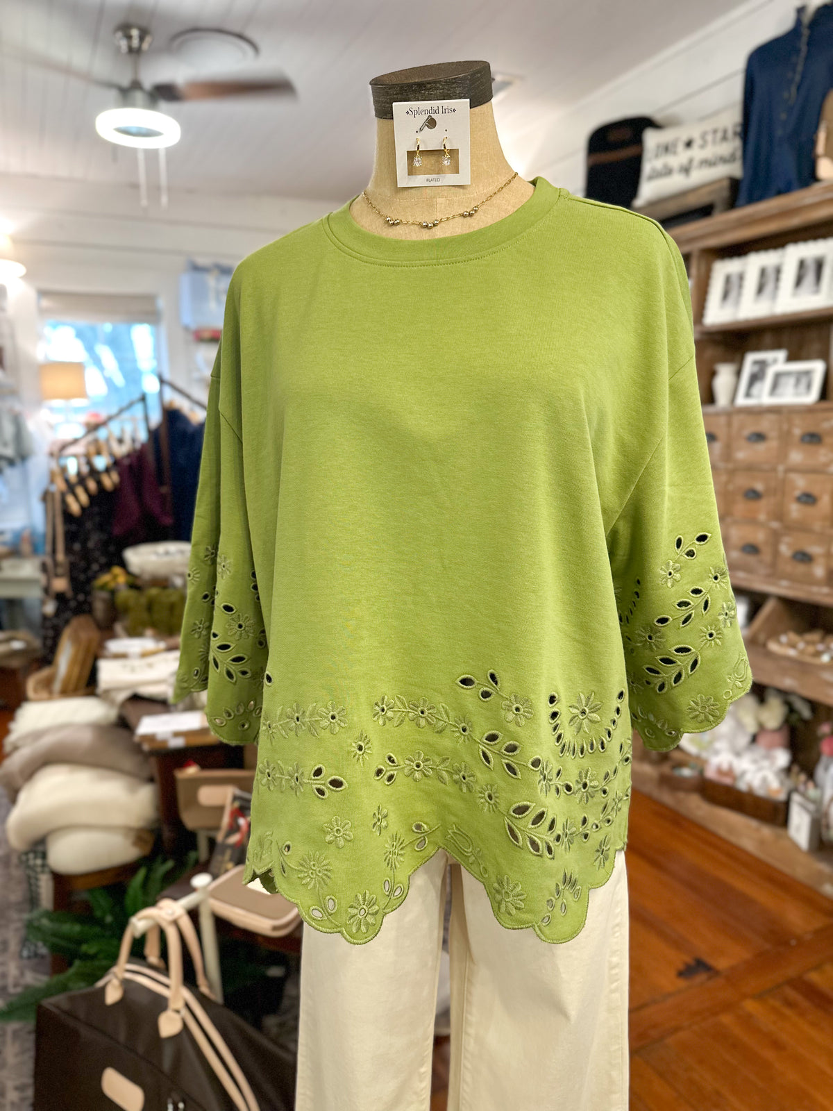 A lime green short-sleeve top with floral eyelet embroidery and a scalloped hem, displayed on a mannequin torso inside a retail store.