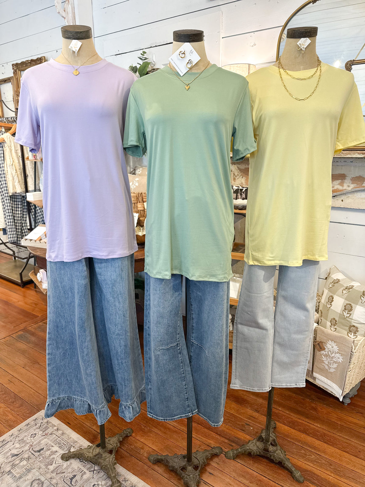 Three mannequins wearing pastel-colored tops and jeans in a store setting.