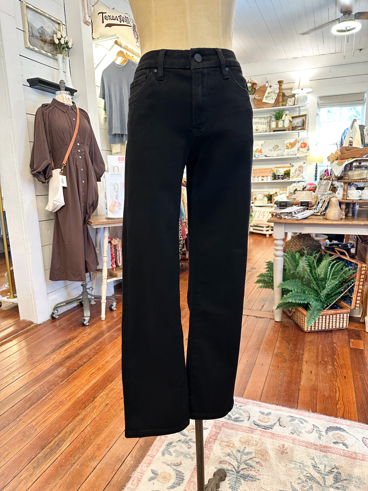 Black pants on a mannequin in a store setting with wooden floors and various items in the background.