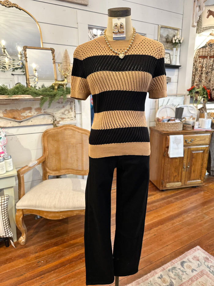 Mannequin wearing a striped sweater and black pants in a room with wooden furniture and decorative items.