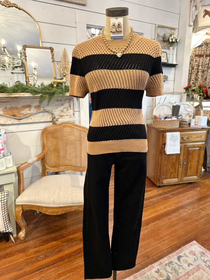 Mannequin wearing a striped sweater and black pants in a room with wooden furniture and decorative items.