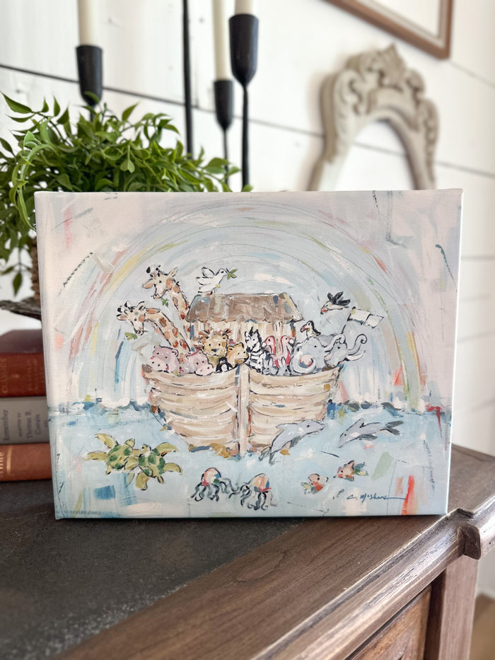 Canvas print of a Noah's Ark painting on a wooden surface with a plant and mirror in the background.