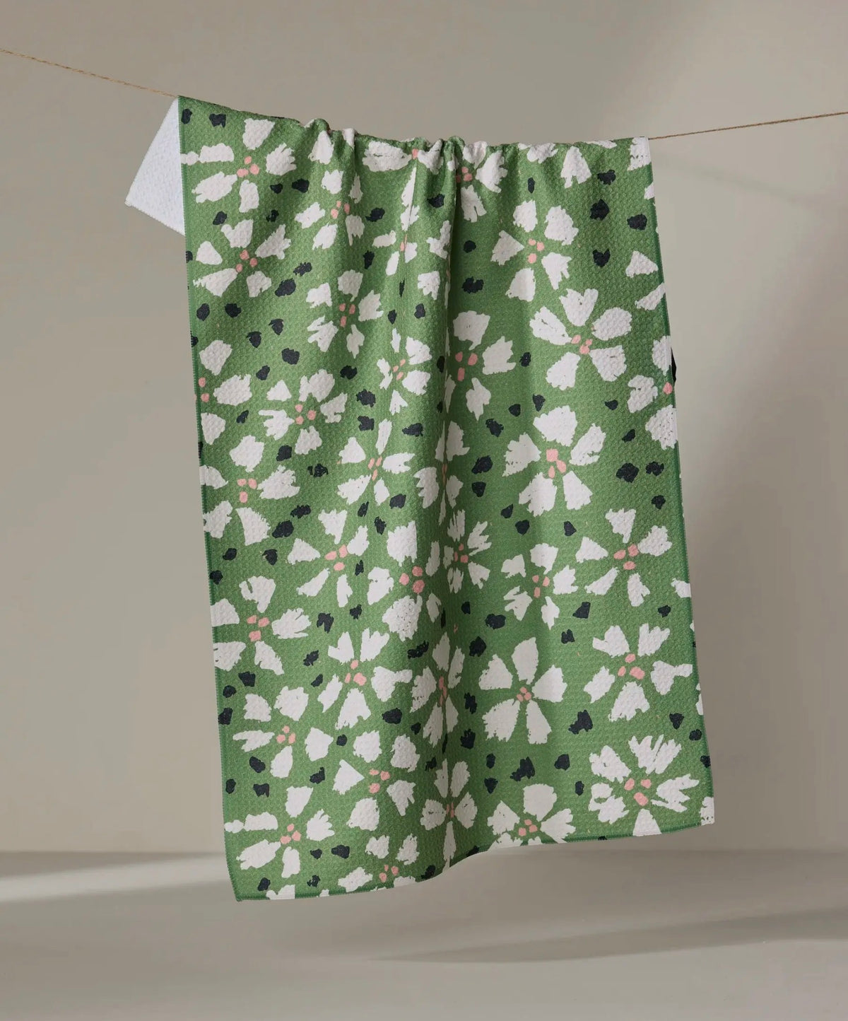 Green fabric with white floral pattern hanging on a line against a neutral background