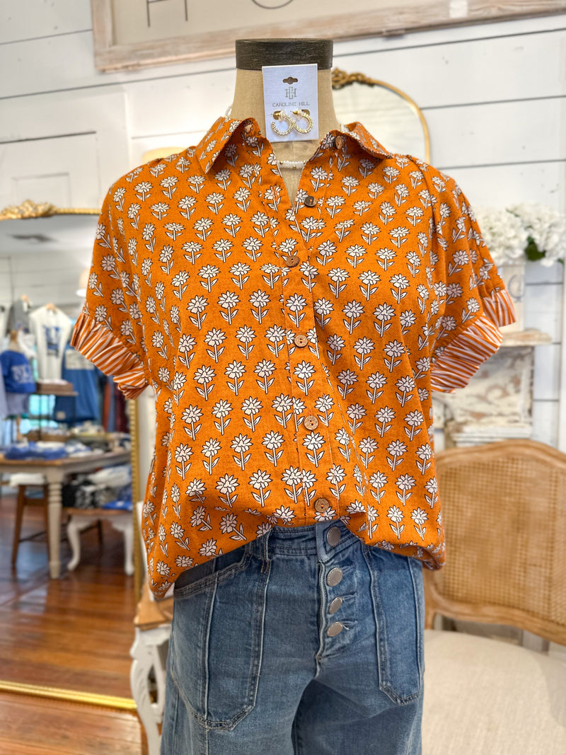 Orange floral patterned shirt on a mannequin with jeans in a store setting layerz clothing stevie top 