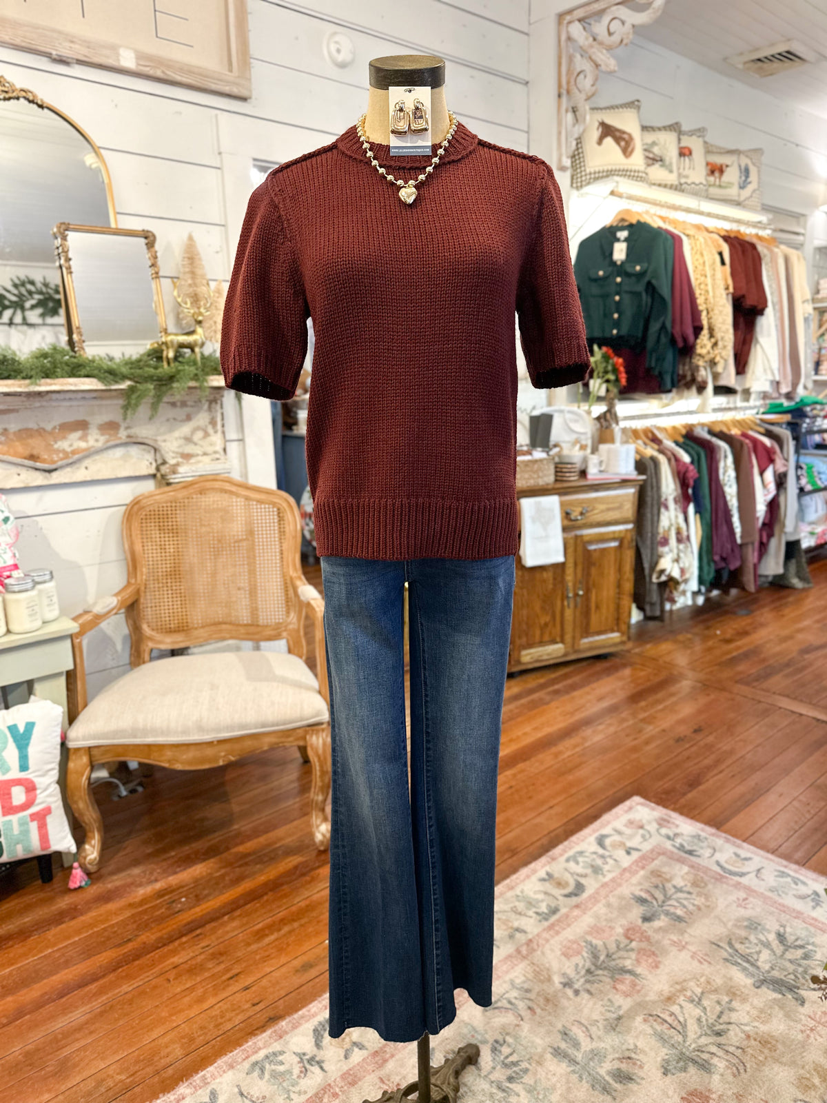 Mannequin wearing a brown sweater and blue jeans in a store setting with furniture and decor.