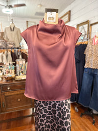 A sleeveless dusty rose satin top displayed on a dress form in a clothing boutique, paired with a pink and black leopard print skirt.