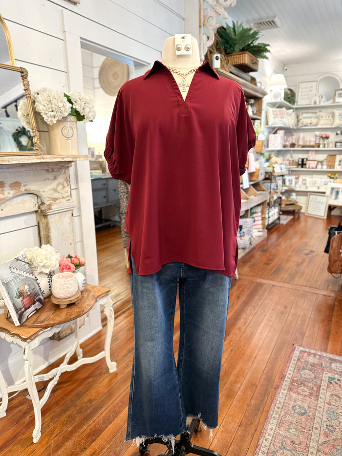 Mannequin wearing a burgundy shirt and blue jeans in a store setting with wooden floors and shelves.