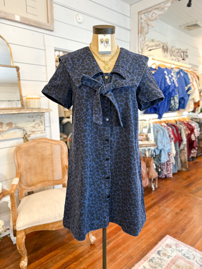 Blue patterned dress on a mannequin in a store setting with wooden floor and chairs.