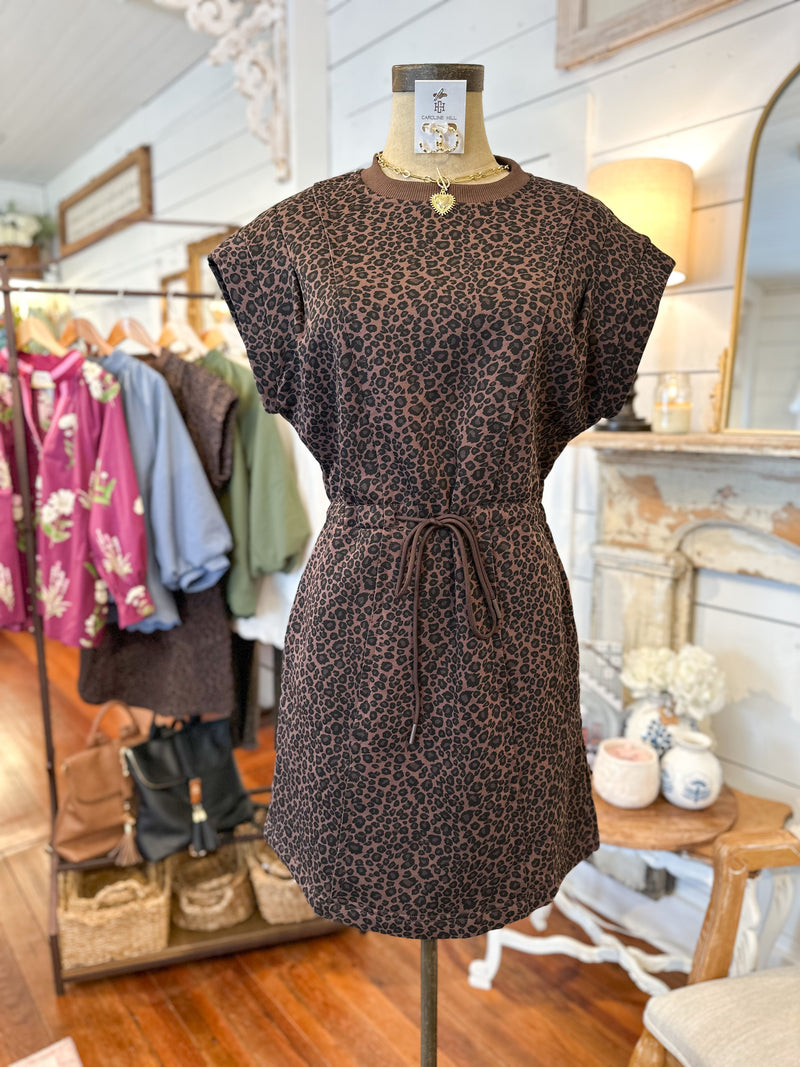 Brown patterned dress on a mannequin in a store setting with clothing racks and decor.