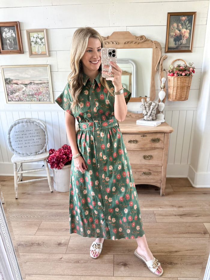 Woman taking a mirror selfie wearing a green floral dress in a home setting.