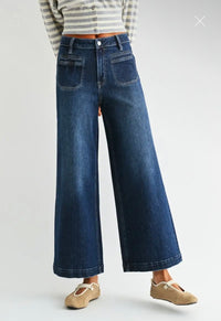 A person wearing dark blue wide-leg denim jeans with a striped long-sleeve top and beige flat shoes, shown from the waist down against a light gray studio background.