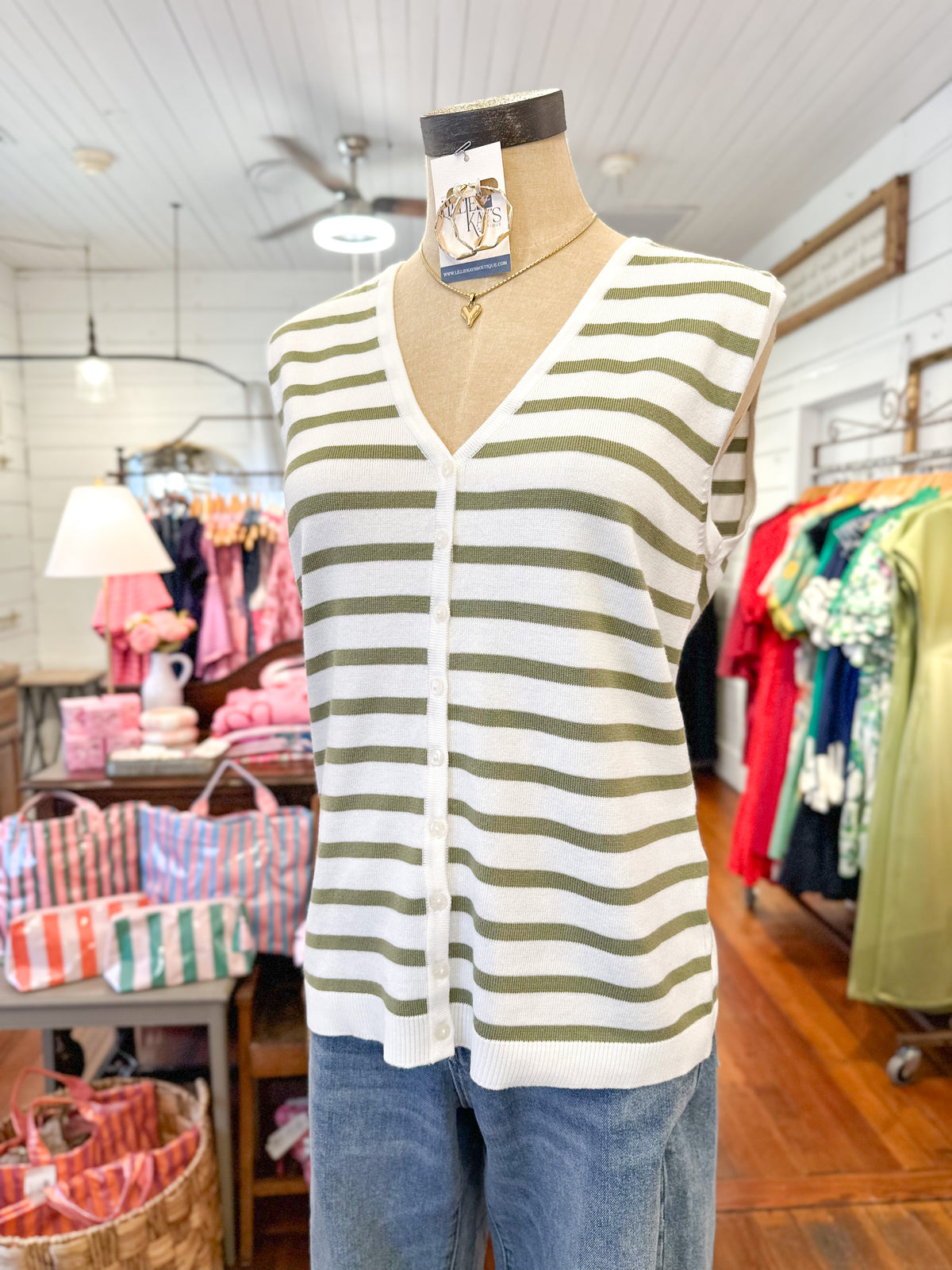 Striped cardigan on a mannequin in a store setting with clothing racks and bags in the background.