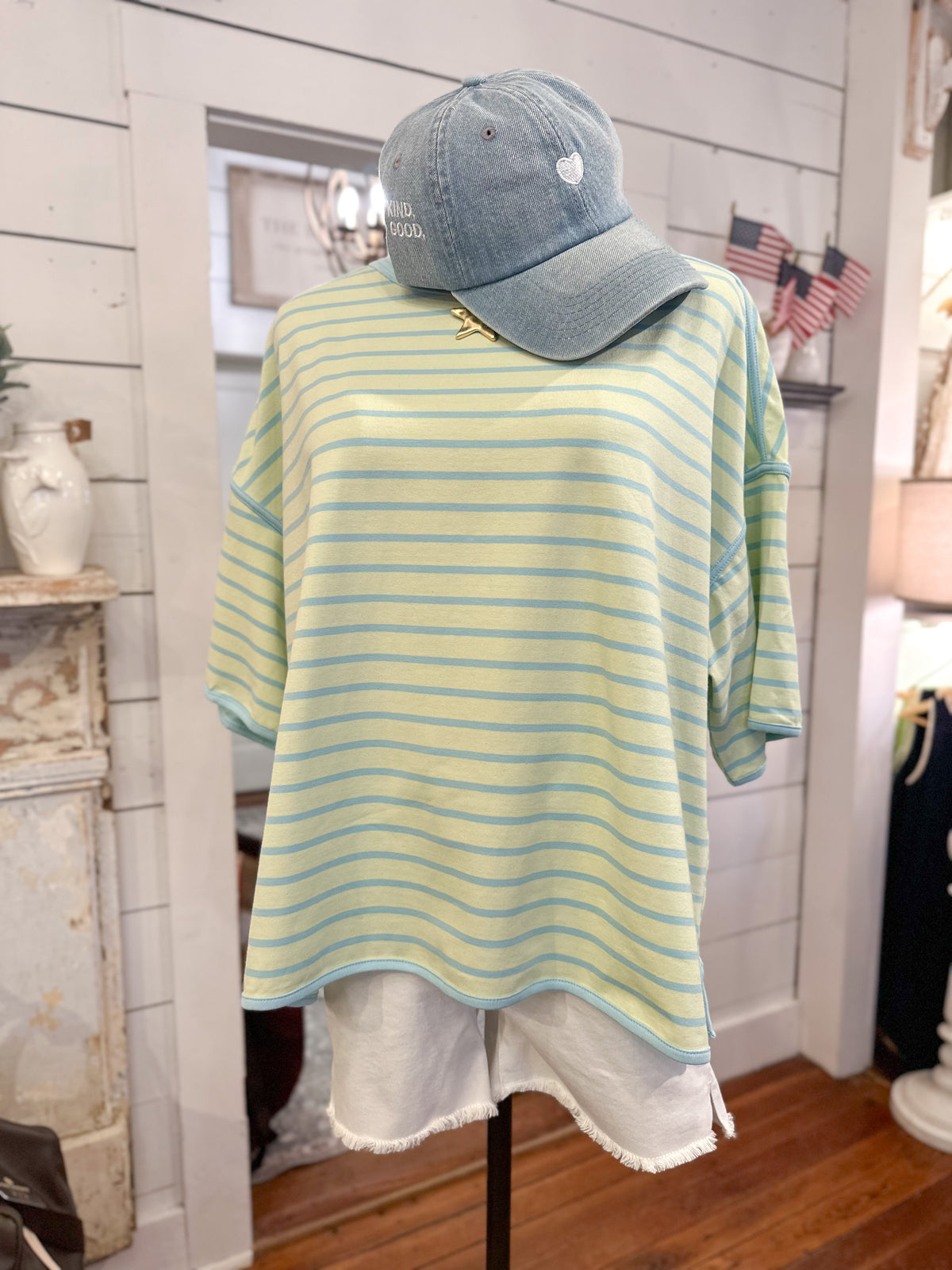 Mannequin wearing a lime green and blue striped shirt with a denim cap indoors.