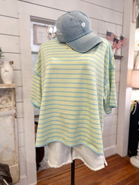 Mannequin wearing a lime green and blue striped shirt with a denim cap indoors.