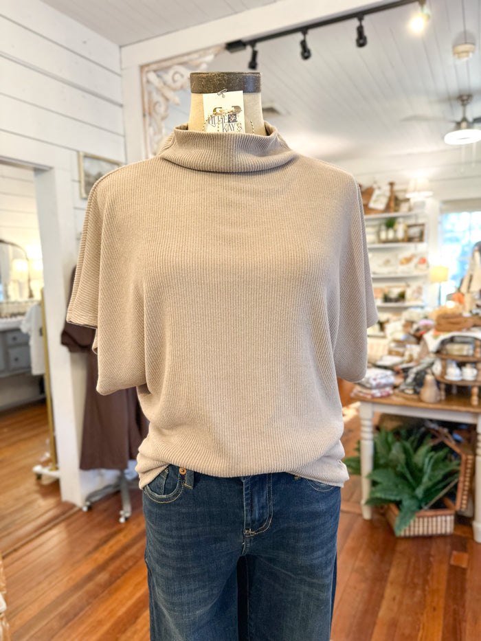 Mannequin wearing a beige turtleneck sweater and blue jeans in a store setting.