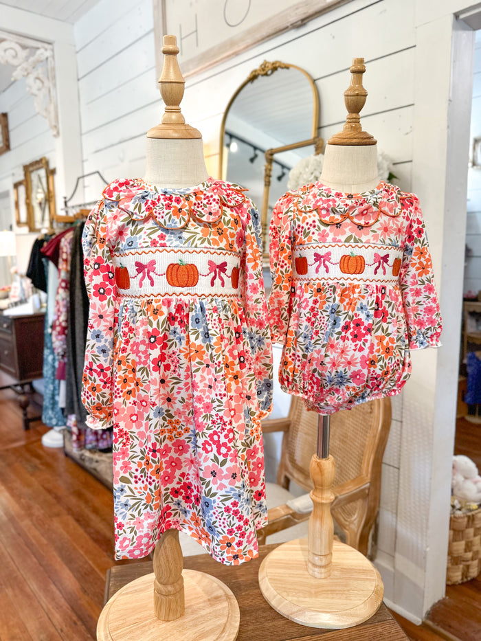 Two floral dresses on mannequins in a store setting with mirrors and clothing racks. pumpkin and bows on outfits 