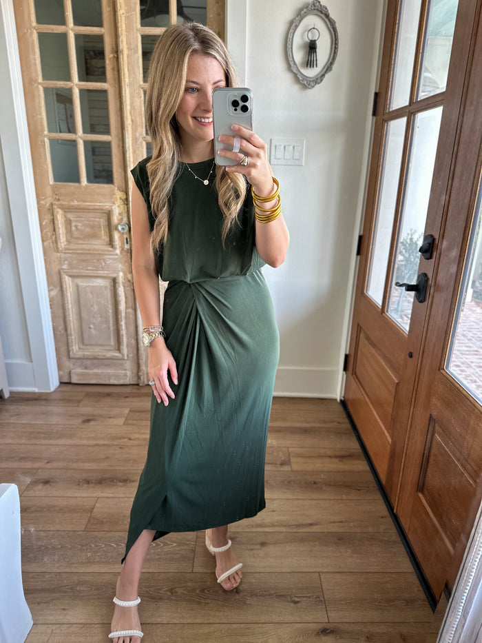 Woman taking a mirror selfie wearing a green dress in a home setting.