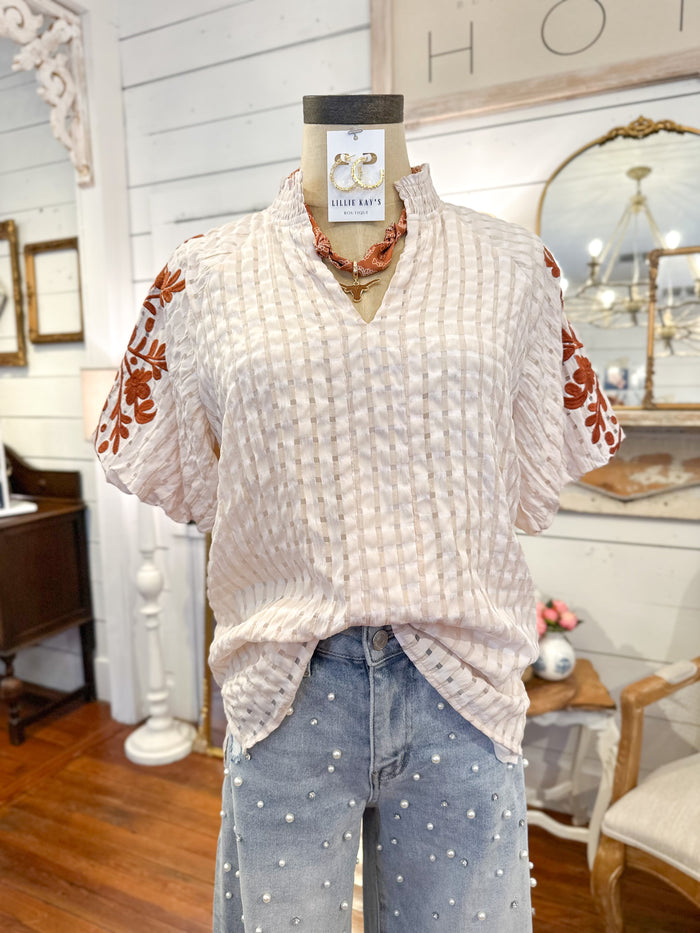 Mannequin wearing a white textured top with floral sleeves in a home decor setting. with pearl jeans 