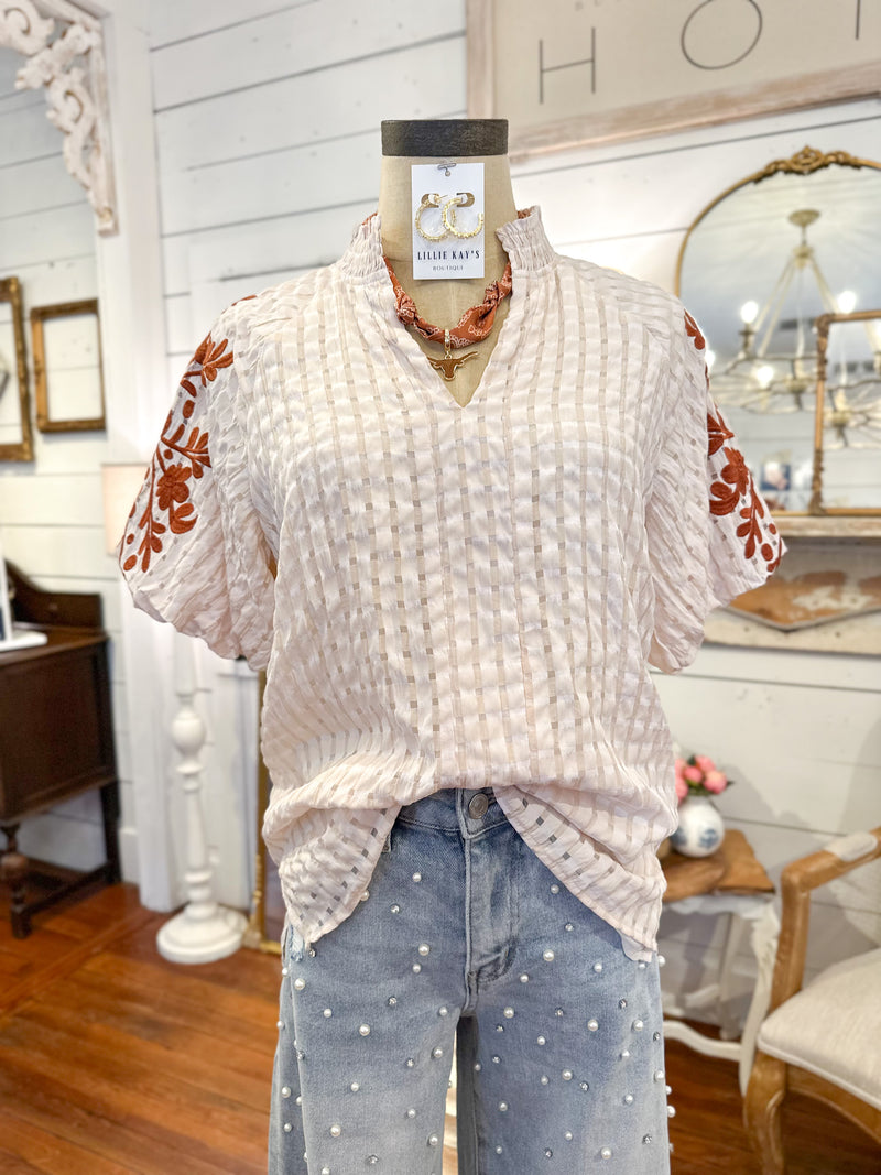 Mannequin wearing a white textured top with floral sleeves in a home decor setting. with pearl jeans 