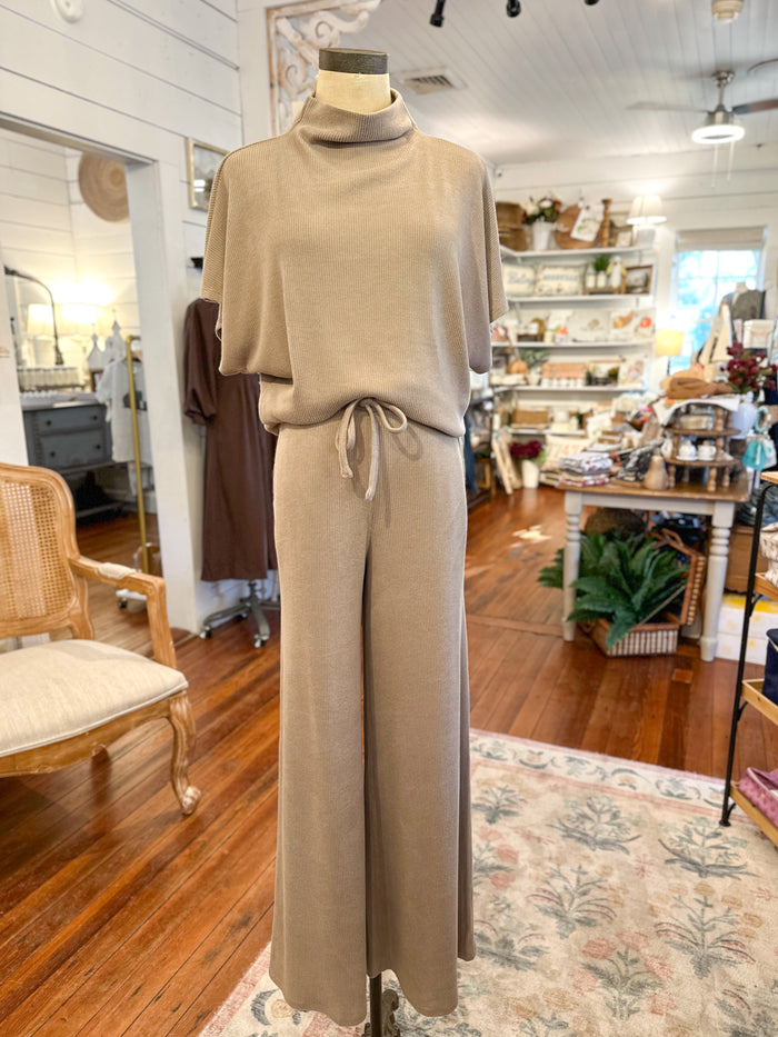 Mannequin wearing a beige outfit in a store setting with wooden floors and shelves.