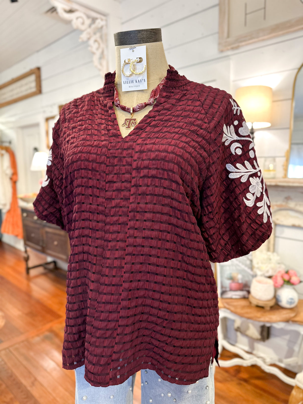 Maroon textured top with white floral patterns on a mannequin in a store setting.