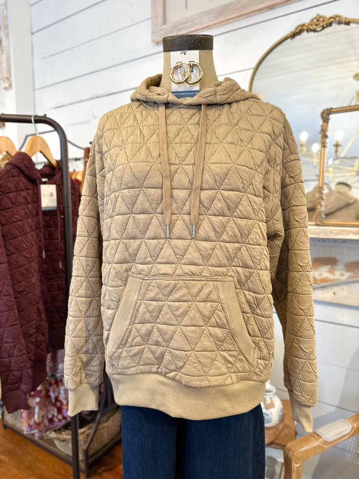 Beige quilted hoodie on a mannequin in a store setting with other clothing in the background.