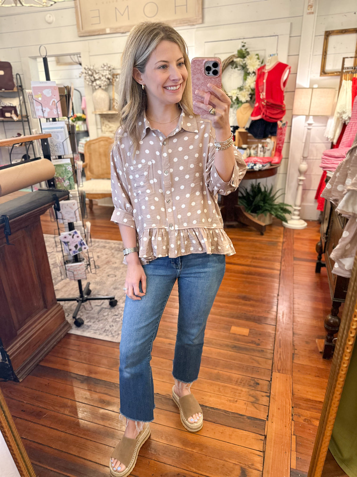 Woman taking a mirror selfie wearing a polka dot blouse and jeans in a store.