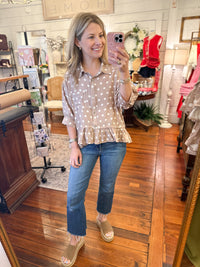 Woman taking a mirror selfie wearing a polka dot blouse and jeans in a store.