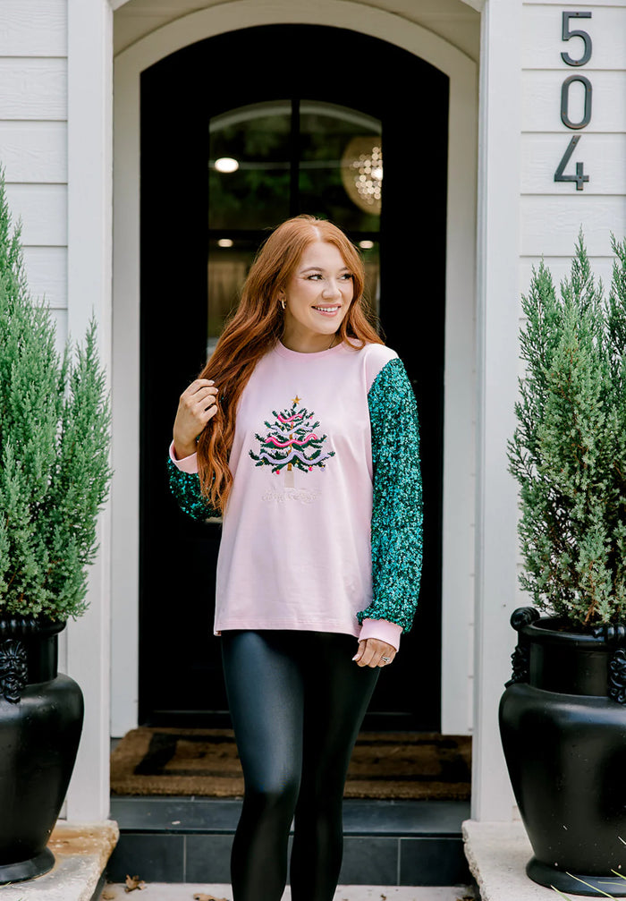 Woman standing outside a house wearing a pink sweater with a watermelon design.