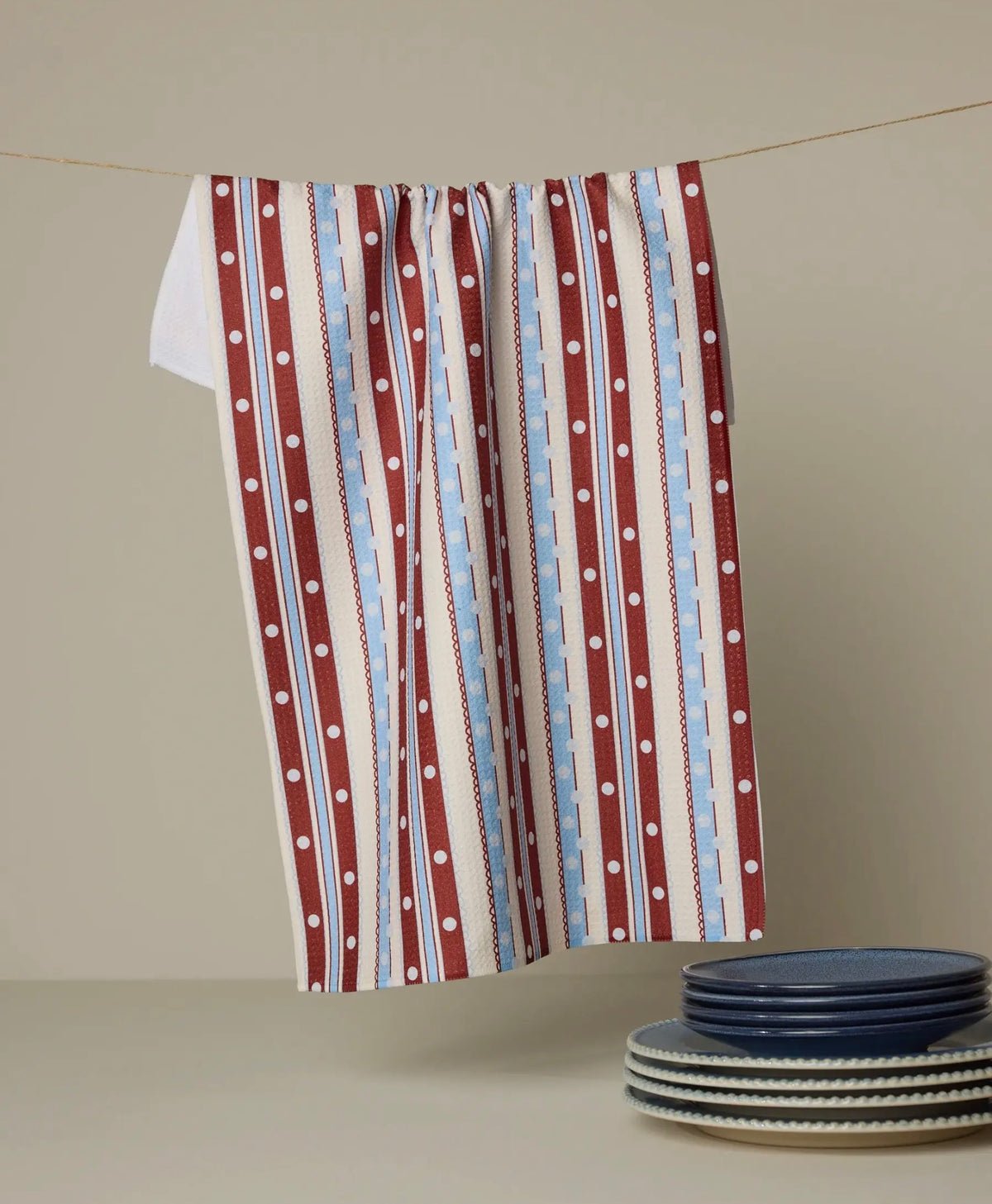 Striped towel with polka dots hanging on a line, with plates stacked below.