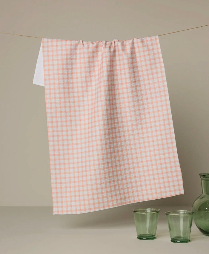 Checkered dish towel on a rod with green glasses and a vase on a neutral background peach color geometry towel 
