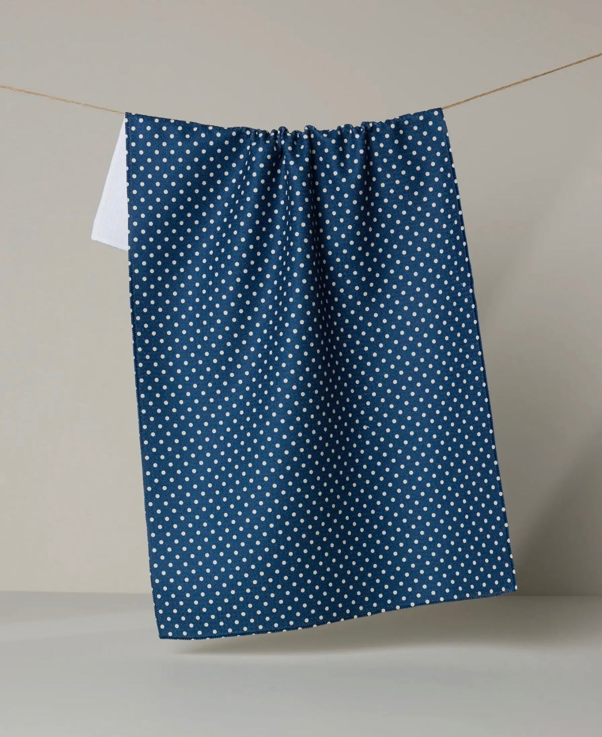 Blue geometry towel with white polka dots hanging on a line against a neutral background