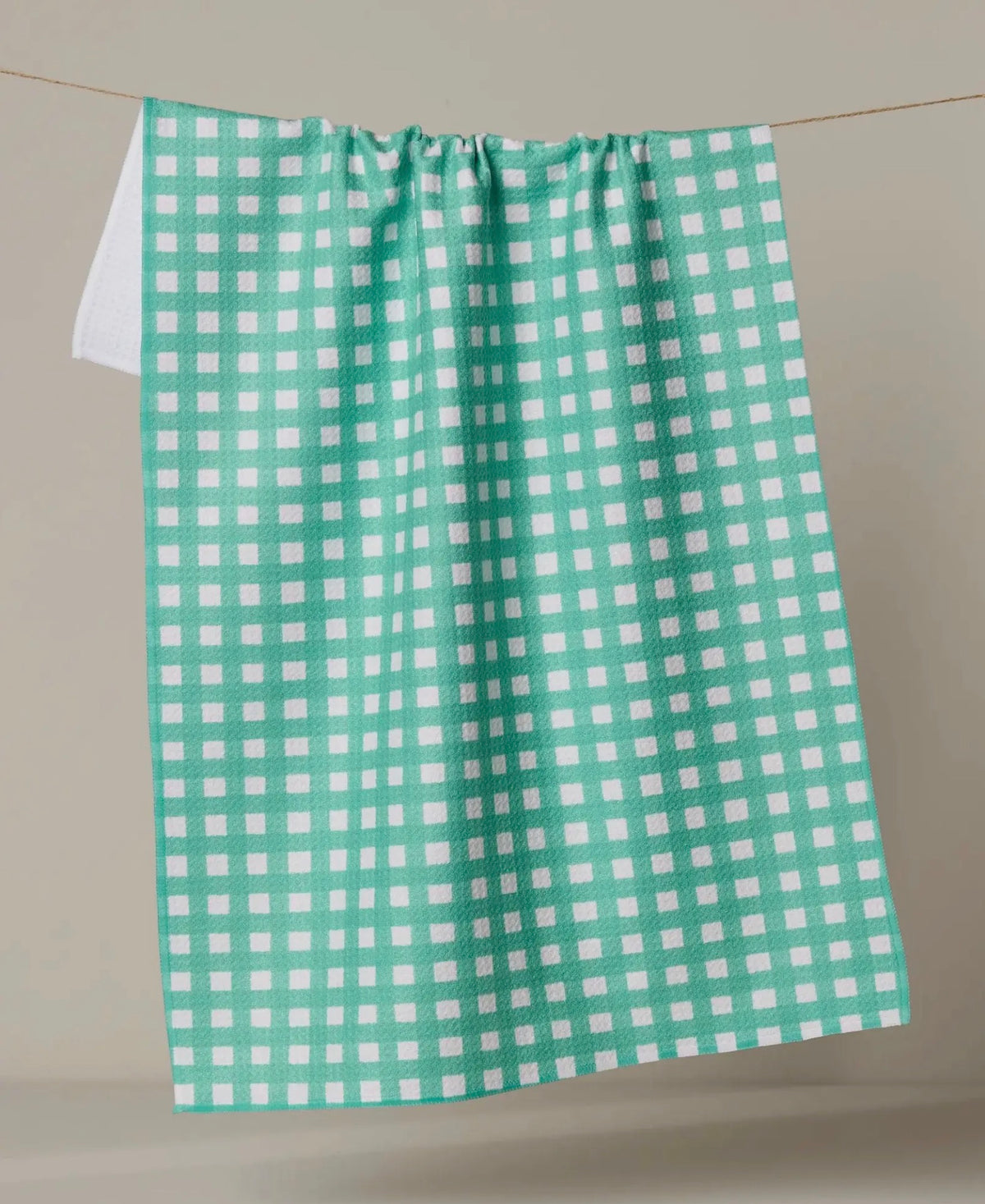 Green and white checkered towel hanging on a line against a neutral background