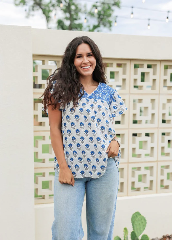 Woman wearing a blue floral top and light blue jeans standing outdoors.