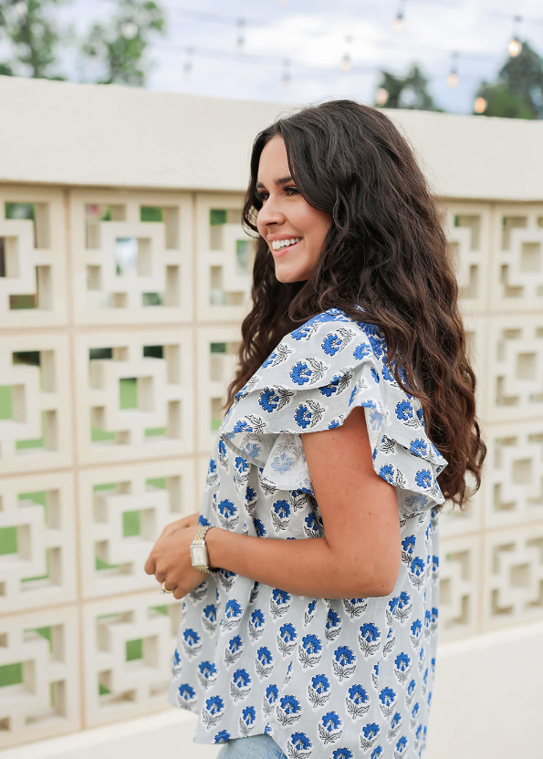 Woman wearing a blue floral dress standing outdoors with a decorative wall in the background LAYERZ CLOTH ALURA TOP 