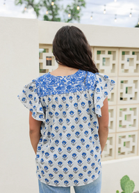 Woman wearing a blue and white floral blouse with a blurred outdoor background