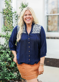 Woman wearing a navy blouse with floral embroidery and a brown skirt 
JANE TOP IN NAVY LAYERZ CLOTHING 