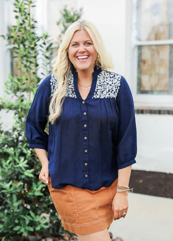 Woman wearing a navy blouse with floral embroidery and a brown skirt 
JANE TOP IN NAVY LAYERZ CLOTHING 
