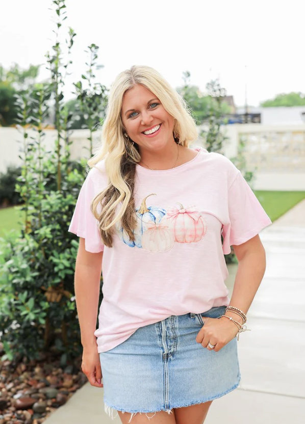 Woman wearing a pink t-shirt with a graphic design and denim skirt outdoors.