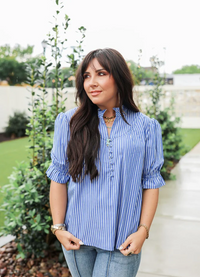Woman wearing a blue striped shirt standing outdoors with greenery in the background
LAYERZ CLOTHING LAUREN TOP 