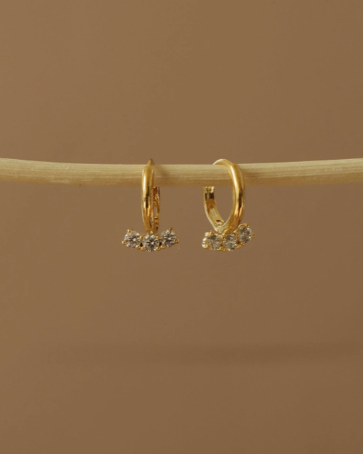 Gold hoop earrings with small stones on a brown background