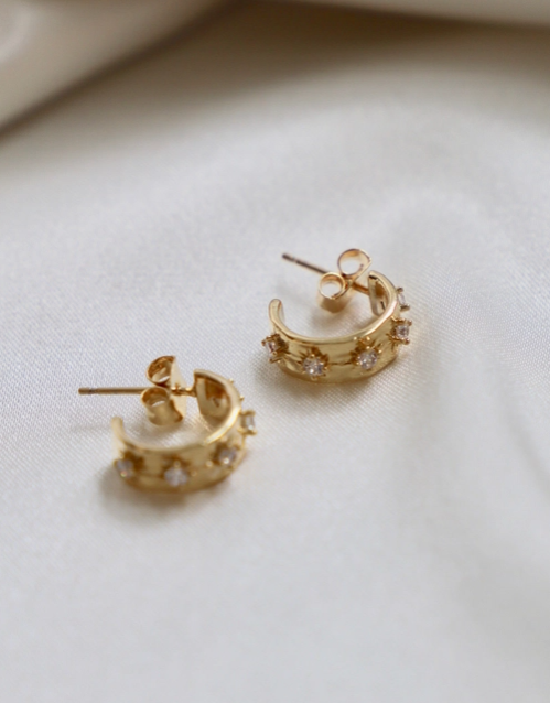 Gold hoop earrings with small stones on a light background