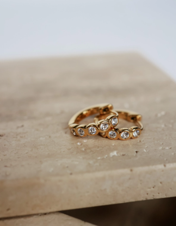 Two gold earring with embedded diamonds on a beige surface