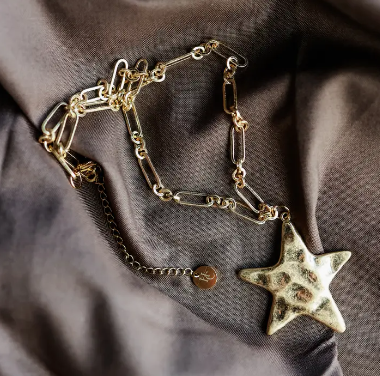 Gold chain necklace with a star pendant on a brown fabric background
