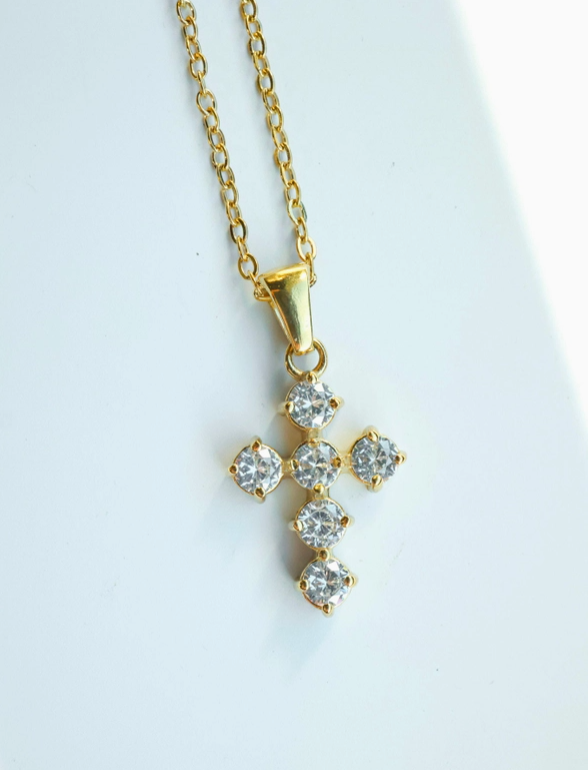 Gold necklace with a diamond like cross pendant on a light gray background